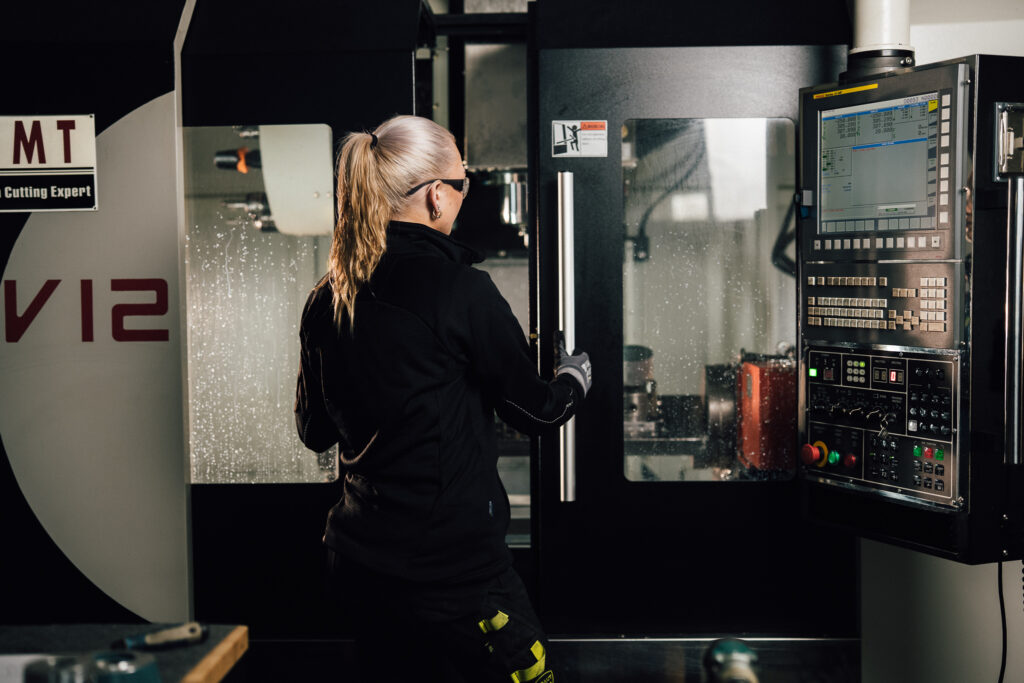 Machinist operating a DMT CNC machine with control panel, wearing protective equipment at Delta Pump
